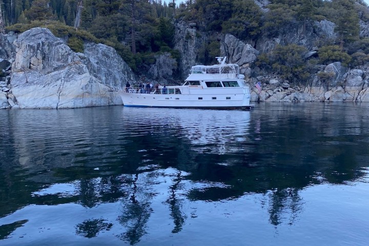 White boat on calm water near rocky shoreline with trees.