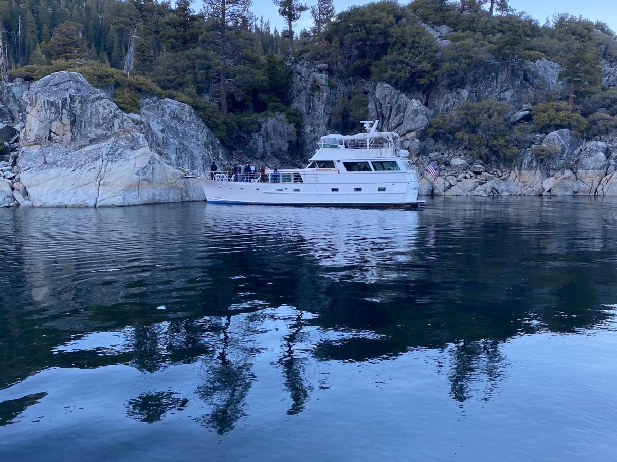 White boat on calm water near rocky shoreline with trees.
