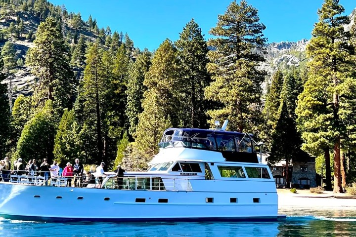 White yacht on blue lake with forest and mountains in background.