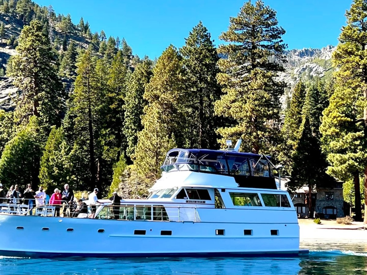 White yacht on blue lake with forest and mountains in background.