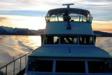 Boat sailing on a calm lake at sunset with mountains in the background.