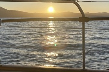 Sunset over ocean seen from railing, mountains in distance