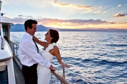 Bride and groom embracing on a boat at sunset, ocean in background.