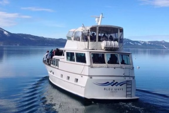 A white ferry boat on a calm lake with mountains in the background.