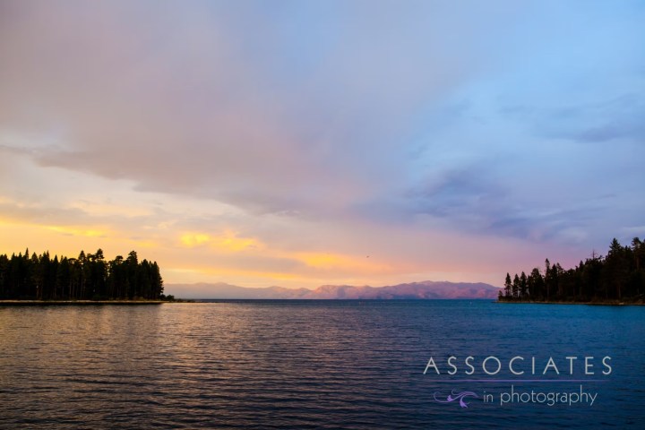 Serene lake at sunset with tree-lined shores and a colorful sky.