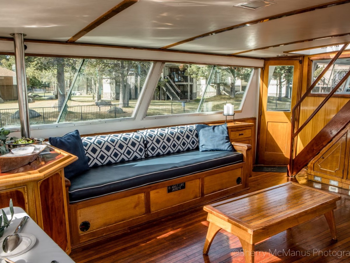 Cozy boat interior with wooden floors, bench seating, and large windows overlooking a dock.